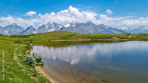 A man jumping at the Koruldi Lake with an amazing view on mountain ridges near Mestia in the Greater Caucasus Mountain Range, Upper Svaneti, Country of Georgia. Reflection in the water. Wanderlust.