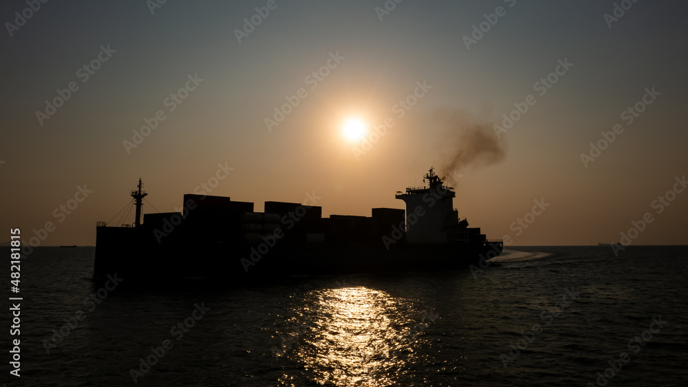Silhouette Container ship full load carrying for import and export, business cargo logistic and transportation by container ship in open sea over the sunlight background,