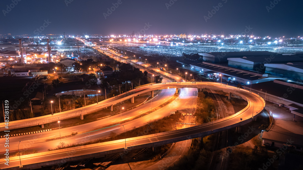 U turn Bridge traffic transportation at night over lighting and factory zone with Commercial shipping port import export international background, drone of point view U turn Bridge traffic transportation at night over lighting and factory zone with Commercial shipping port import export international background, drone of point view
