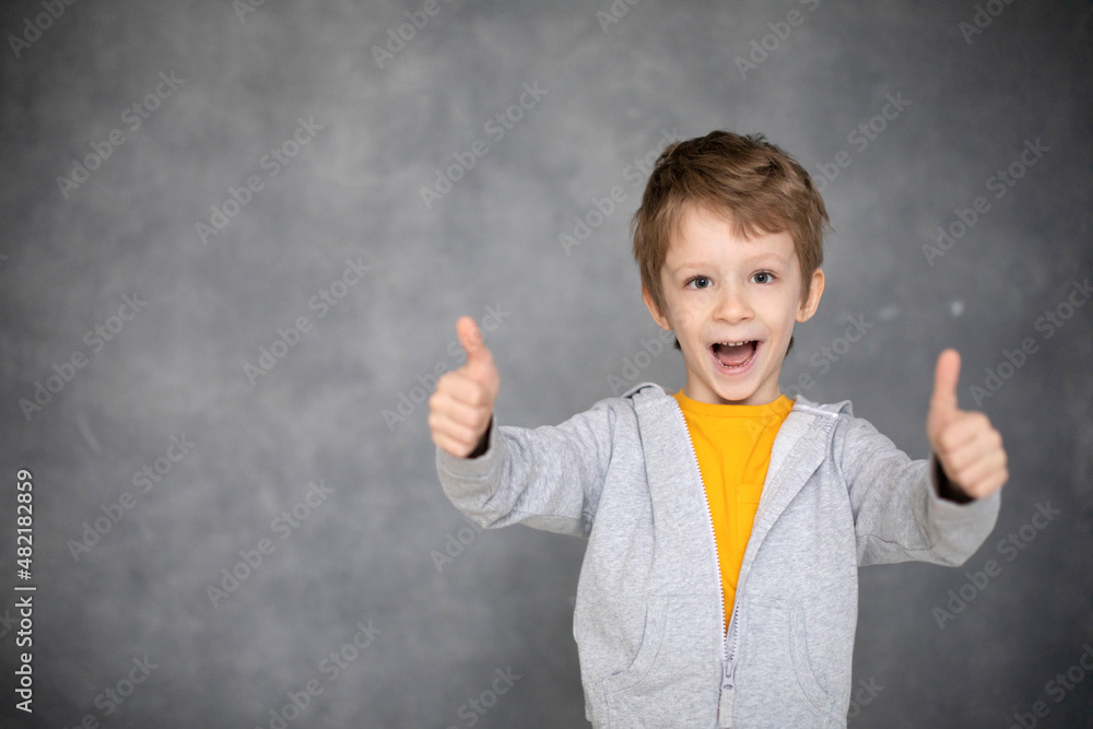 Portrait of beautiful happy little boy giving thumbs up on modern gray background. Portrait of beautiful happy little boy giving thumbs up on modern gray background.