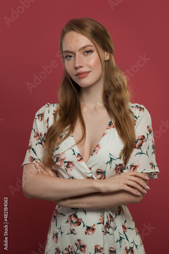 Young redhead woman with arms crossed on red background