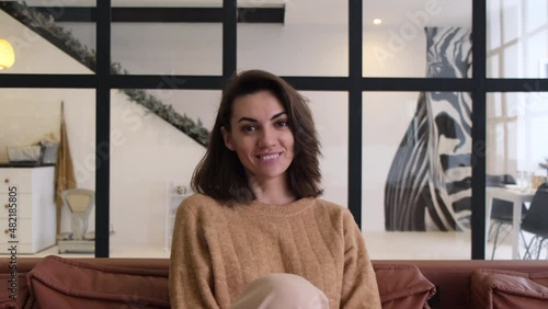 Young woman sitting at home on the couch in a good mood looking at the camera and smiling cheerfully 