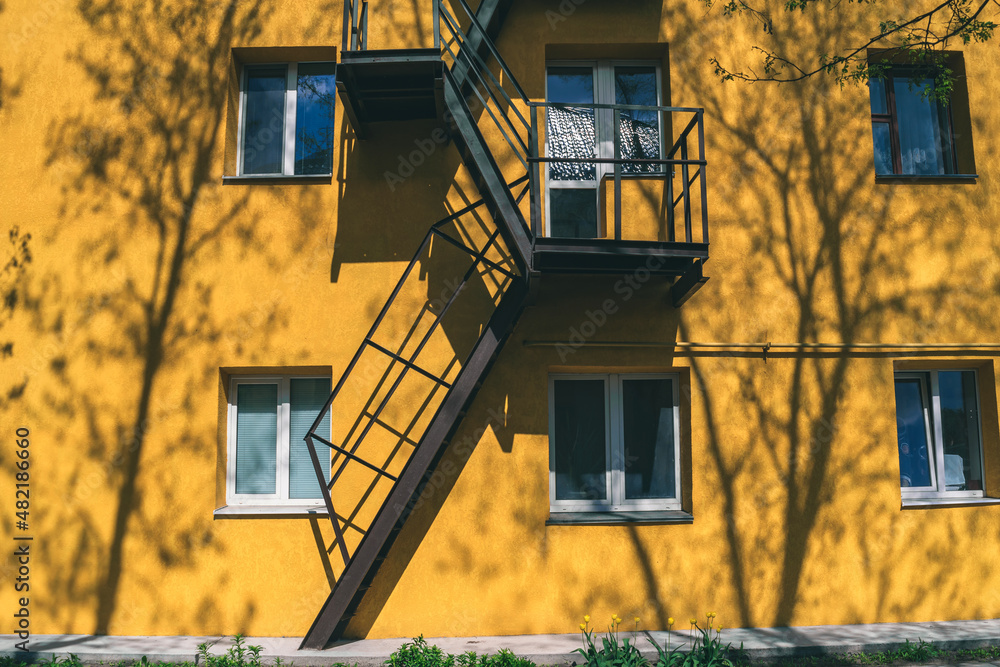 Yellow house with windows and a fire escape with tree shadows. Yellow house with windows and a fire escape with tree shadows.