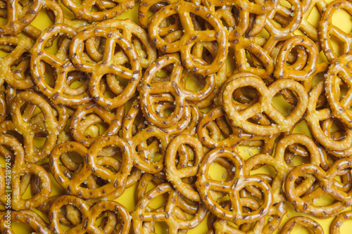 pile of salty mini pretzels on a yellow background. Popular beer snack. Background of baked salted pretzels. Top view