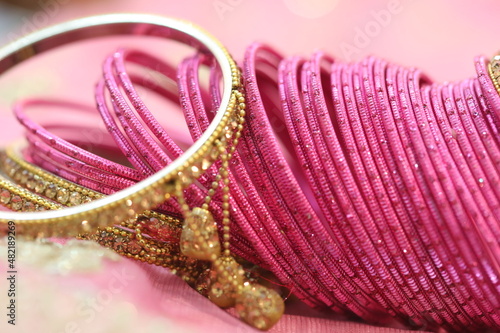 close up of gold bangle and dozens of pink glass decorative bangles spread on pink saree photo