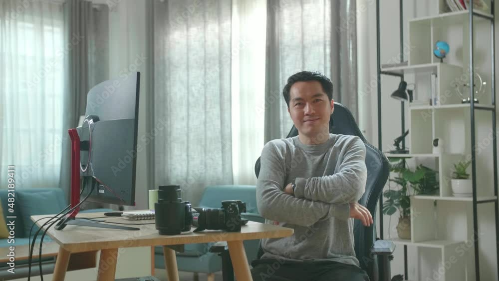Asian Cameraman In Long Sleeved T-Shirt And Black Pants Crossing His Arms And Smiling To Camera While Working With Desktop Computer At Home.
Asian Cameraman In Long Sleeved T-Shirt And Black Pants Crossing His Arms And Smiling To Camera While Working With Desktop Computer At Home.