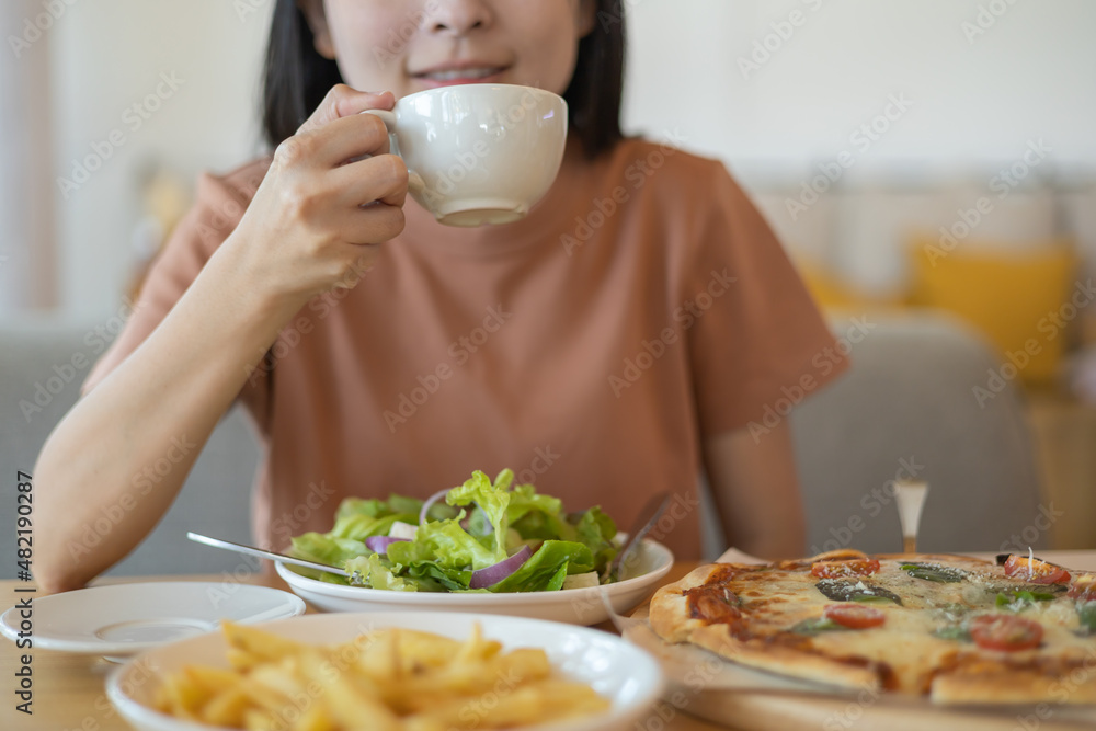 A woman drinking coffee with feeling happy and enjoy to eat food in the restaurant in leisure time. dine in the restaurant, eating delicious served hot pizza and salad. Eating concept. Italian food.