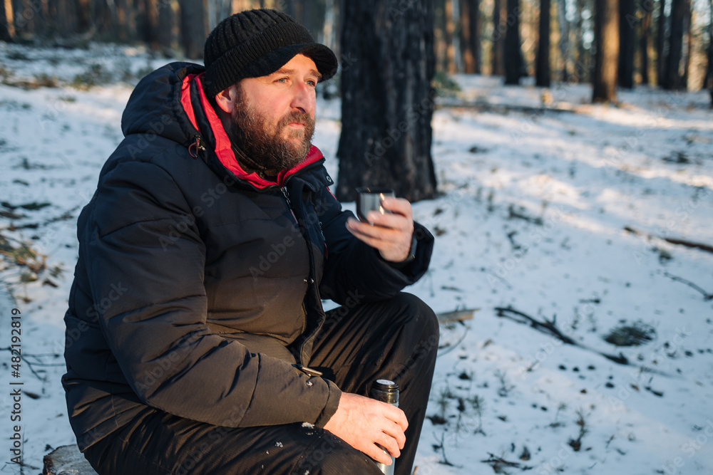pensive bearded man in the winter forest sits and drinks tea pensive bearded man in the winter forest sits and drinks tea
