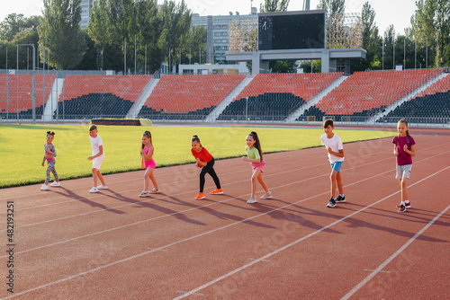 A large group of children, boys and girls, run and play sports at the stadium during sunset. A healthy lifestyle. © Andrii