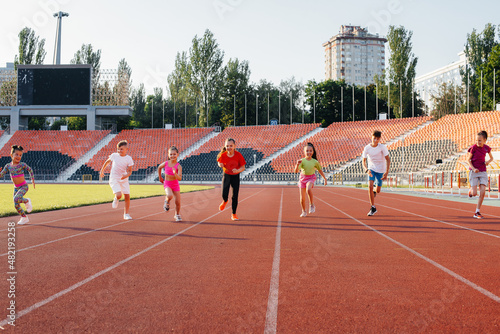 A large group of children, boys and girls, run and play sports at the stadium during sunset. A healthy lifestyle.