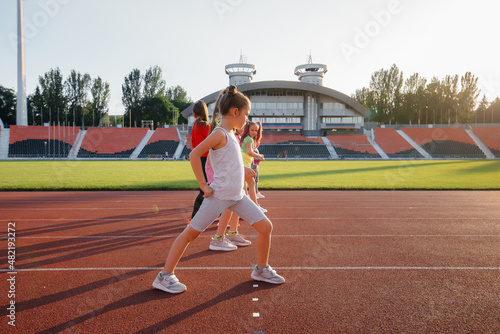 A large group of girls, got ready at the start before running at the stadium during sunset. A healthy lifestyle. © Andrii