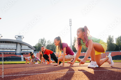 A large group of girls, got ready at the start before running at the stadium during sunset. A healthy lifestyle. © Andrii