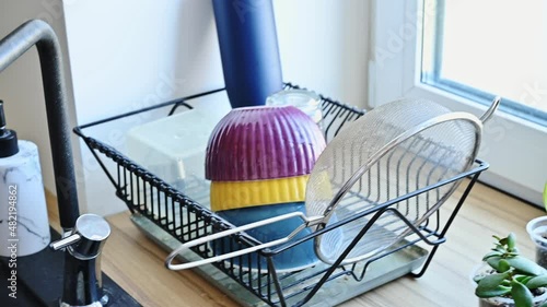 Woman washing a bowl in the kitchen sink and then putting it to dry in a dish drainer or plate rack photo