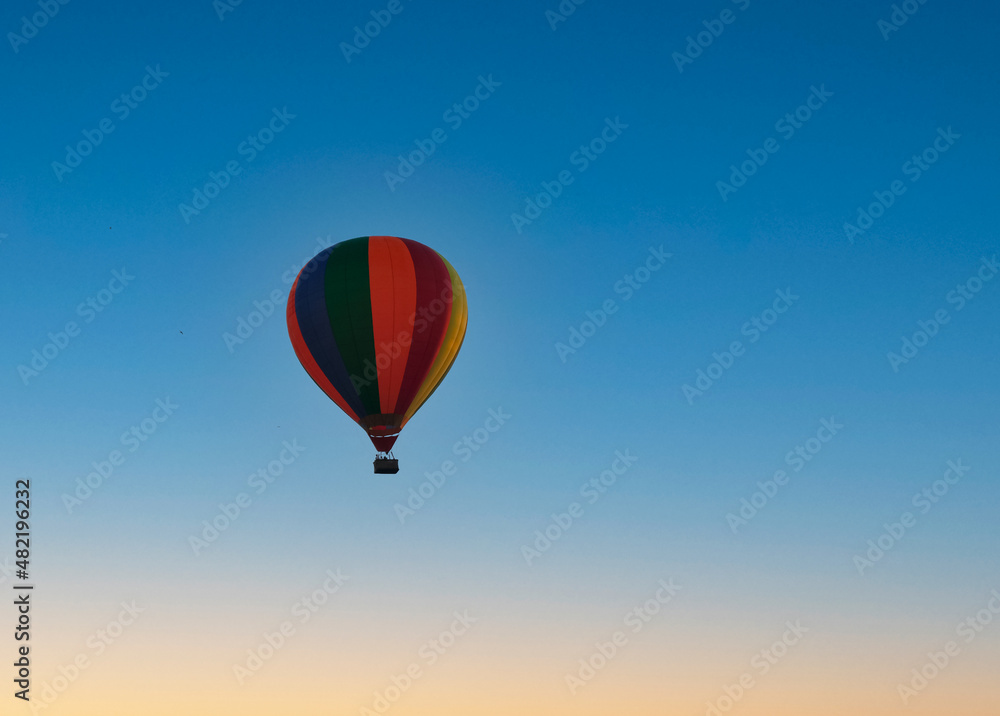 Fototapeta premium Colorful hot air balloon flying through the sky while the sun is setting
