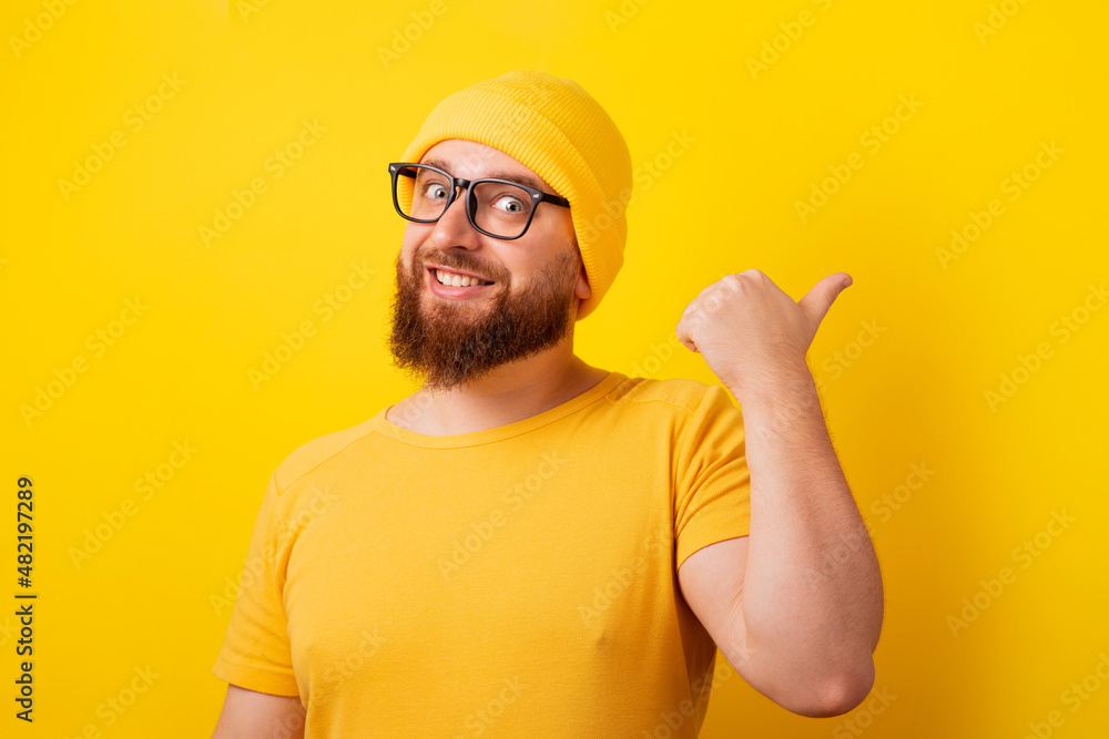 smiling man showing thumb up gesture and pointing at empty space  over yellow background