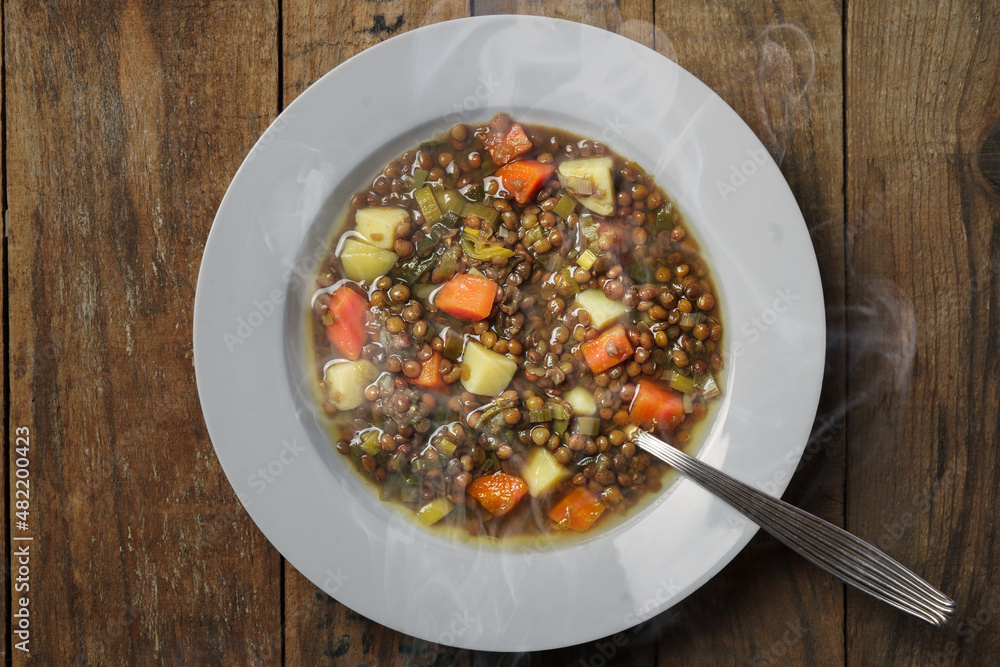 Steaming lentil soup on a plate with a spoon on wooden background