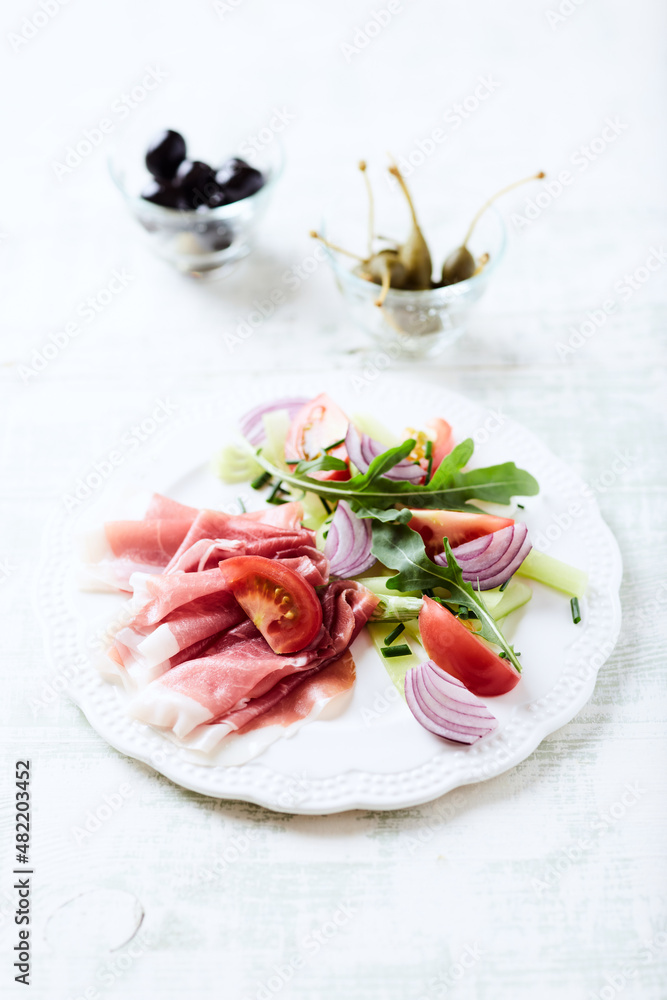 Plate of smoked ham with tomatoes and rocket. Bright wooden background.