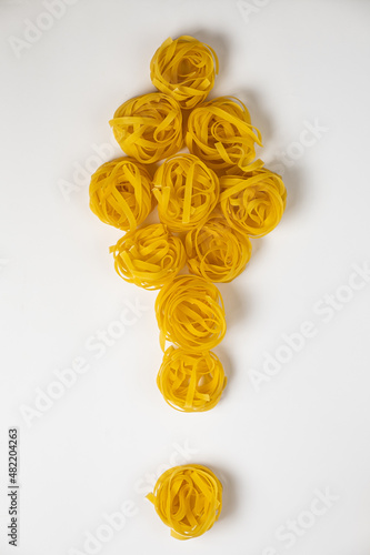 few homemade fettuccine nest in the shape of a exclamation mark isolated on white background