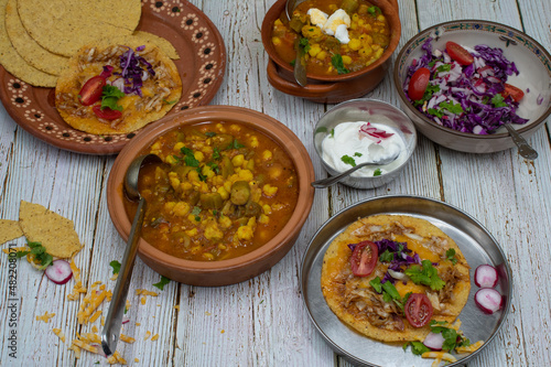 Vegetarian okra pozole and corn quesadillas in traditional Mexican clay dishes, wooden table.