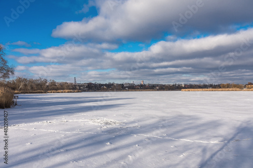 The frozen lake begins to melt on a sunny day. Industry landscape. Human footprints on a frozen lake. Beautiful white clouds over a frozen lake. Snow.