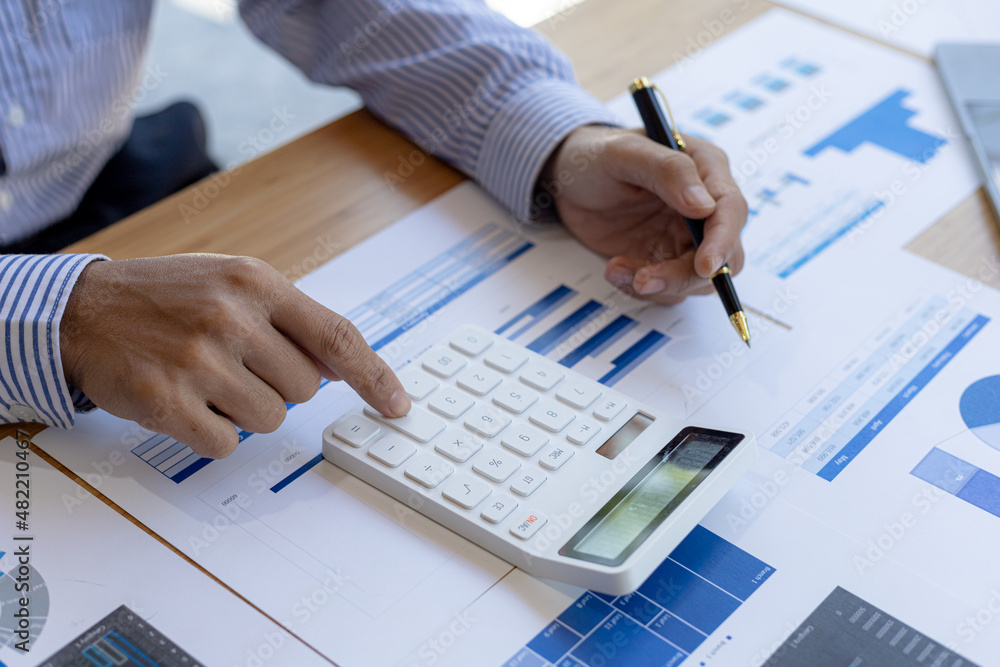Businessman using a calculator to calculate numbers on a company's financial documents, he is analyzing historical financial data to plan how to grow the company. Financial concept. Businessman using a calculator to calculate numbers on a company's financial documents, he is analyzing historical financial data to plan how to grow the company. Financial concept.