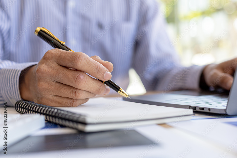 Businessman takes notes in a notebook, owns a startup company, sits in his office and checks the company's financial summary prepared by the finance department. Management concept of startup company. Businessman takes notes in a notebook, owns a startup company, sits in his office and checks the company's financial summary prepared by the finance department. Management concept of startup company.