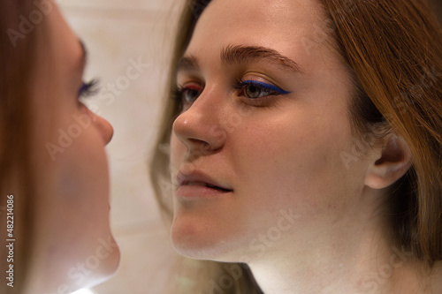 Young woman with white skin reflection in the mirror used blue eyeliner