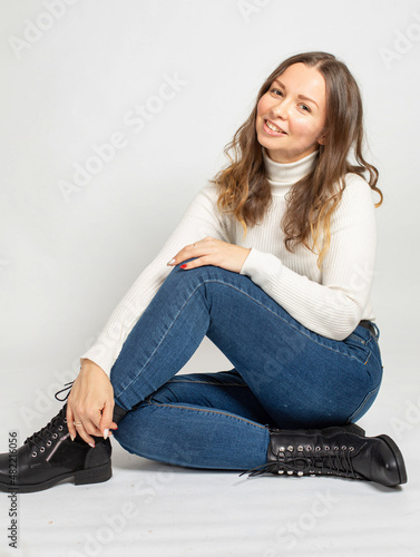 Attractive young european woman in warm white jumper isolated on white sitting on the floor