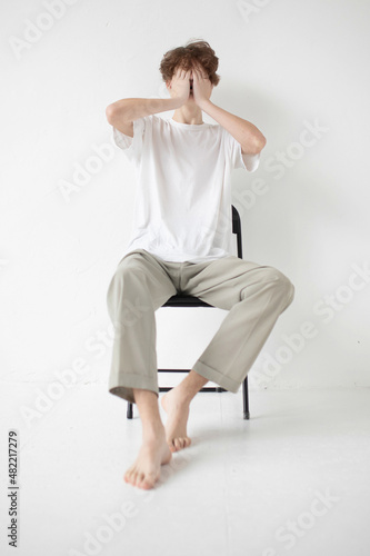 Barefoot attractive young european man isolated on light grey covered his face by hands sitting on chair