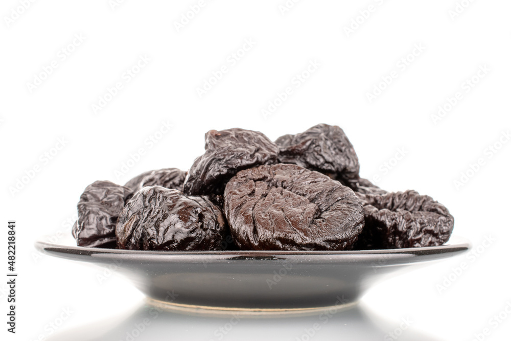 Several organic sweet prunes on a black saucer, macro, isolated on white. Several organic sweet prunes on a black saucer, macro, isolated on white.