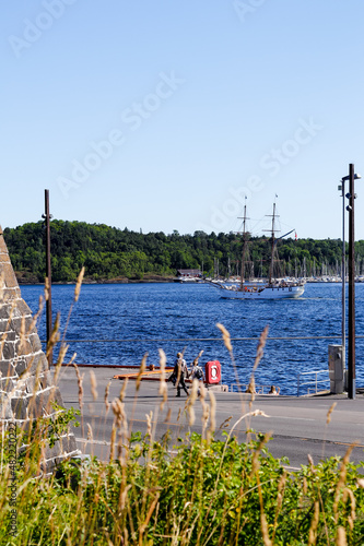 Adult and child walking along the harbour, looking at a sailing boat in the Oslo Fjord