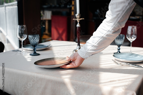 A young waiter in a stylish uniform is engaged in serving the table in a beautiful gourmet restaurant close-up. Table service in the restaurant.