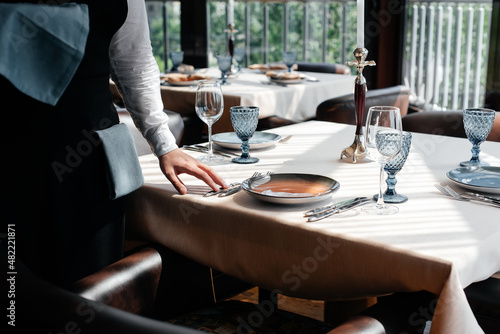 A young waiter in a stylish uniform is engaged in serving the table in a beautiful gourmet restaurant close-up. Table service in the restaurant.