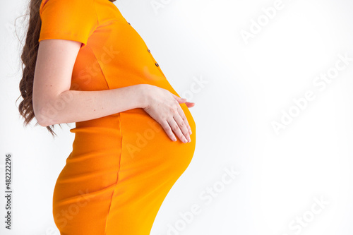 Pregnant woman in a bright orange dress hugs her belly