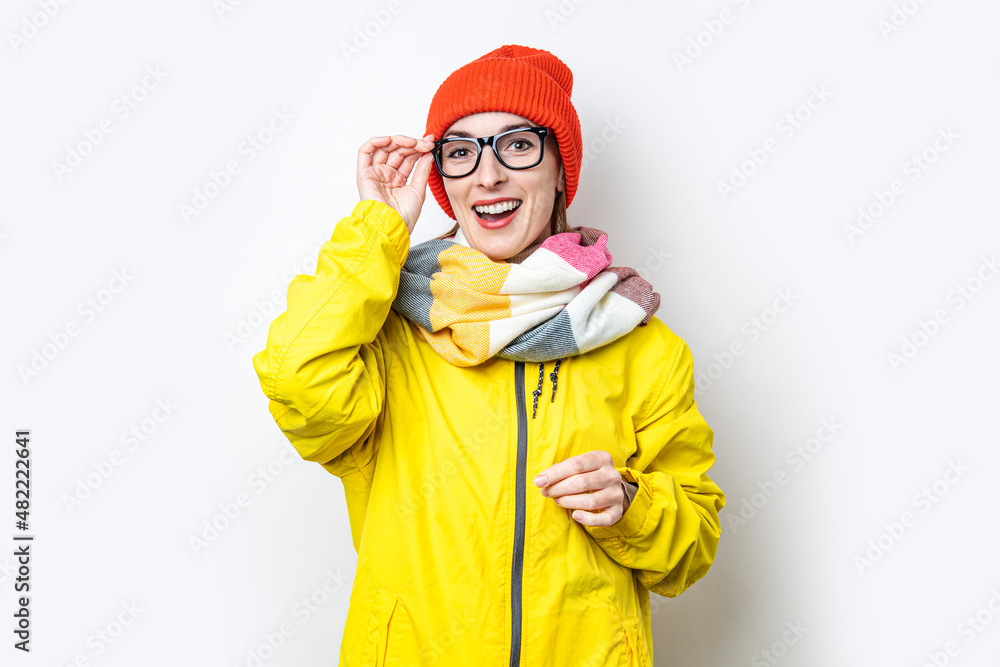 Cheerful young girl in glasses, in a yellow jacket on a light background.