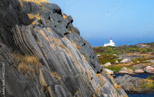 Stone wall on an island, with a lighthouse in the background. Sunlight, summer