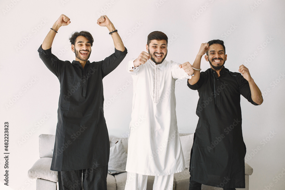Three indian men standing near coach and watching football on laptop Three indian men standing near coach and watching football on laptop