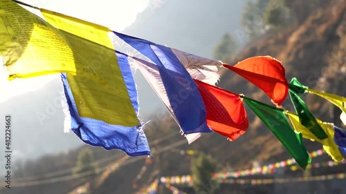 Slow motion shot of colorful Buddhist Tibetan prayer flag in front of mountains at Pangan Nyingmapa Monastery in Patlikuhal village near Manali, Himachal Pradesh, India	