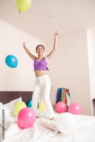 Happy young woman jumping on bed with balloons at home