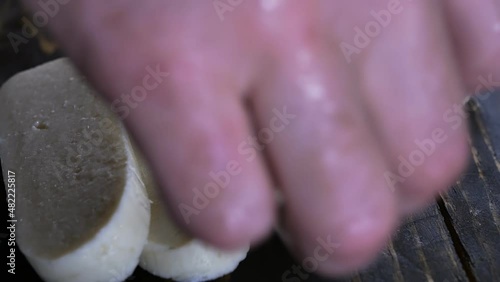 the hand of a male cook stacked sliced pieces of halloumi cheese on a dark wooden board for frying in a pan photo