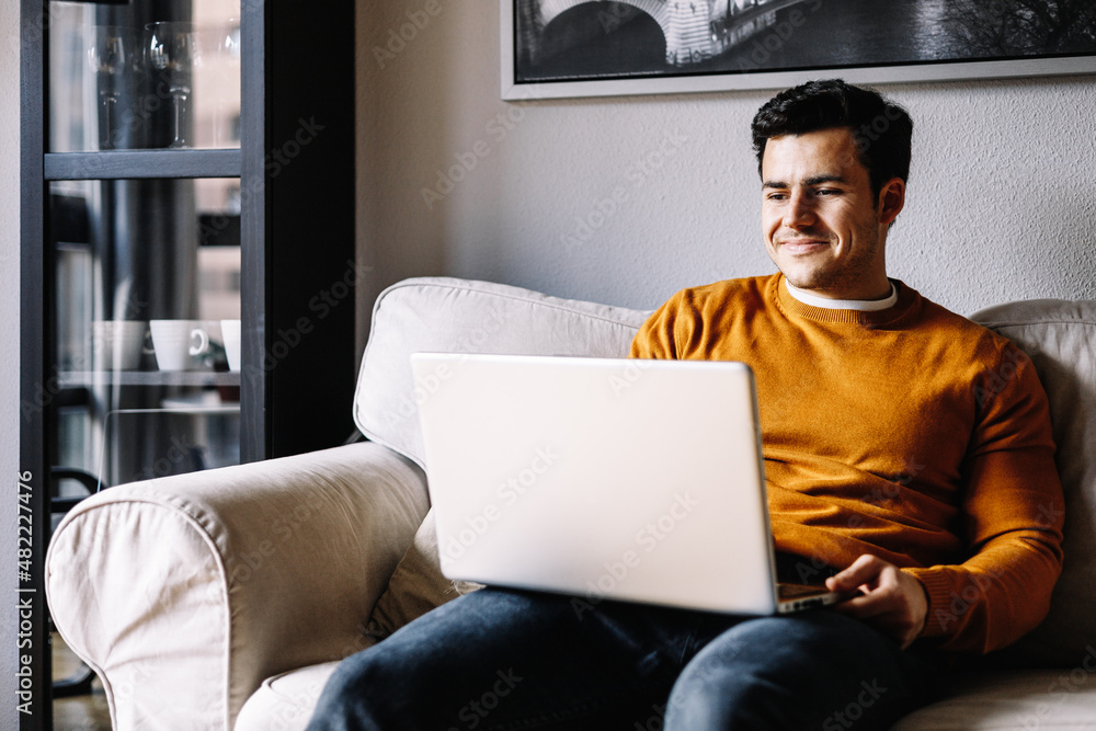 smiling young man using laptop in sofa at home smiling young man using laptop in sofa at home