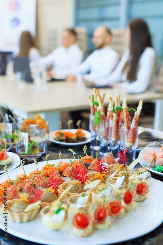 Catering in the office. A table with canapes and various snacks served  on the background of a business meeting.