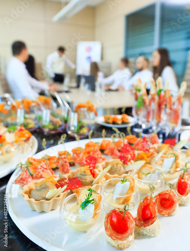 Catering in the office. A table with canapes and various snacks served  on the background of a business meeting.