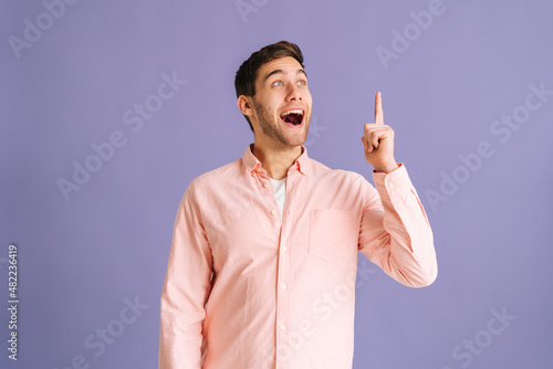 Portrait of happy young man thinking about something and having idea moment pointing finger up on pink isolated background. Cheerful male showing eureka gesture in studio. photo