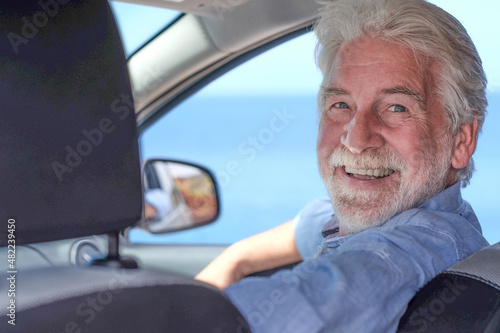 Beautiful senior white-haired man inside his car smiles looking at camera. Horizon over water © luciano