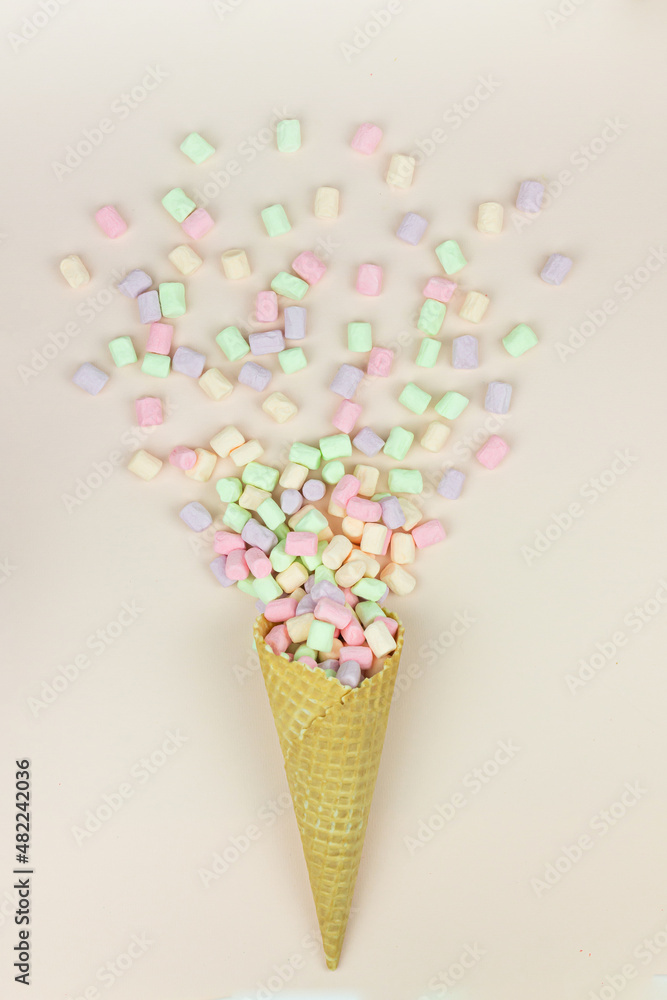Yellow waffle cone with green, pink and yellow marshmallows on pastel background. Yellow waffle cone with green, pink and yellow marshmallows on pastel background.