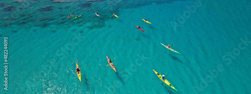 Aerial drone ultra wide panoramic photo with copy space of unidentified caucasian women paddling on tropical island exploring beautiful exotic nature in turquoise calm sea