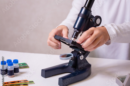 A schoolgirl with a microscope examines chemicals in test tubes, conducts experiments. The concept of coronavirus research in the laboratory