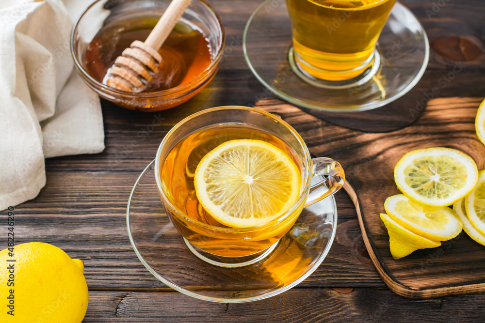 A cup of tea with a slice of lemon and a bowl of honey on a wooden table. Vitamin warming drink. Close-up A cup of tea with a slice of lemon and a bowl of honey on a wooden table. Vitamin warming drink. Close-up