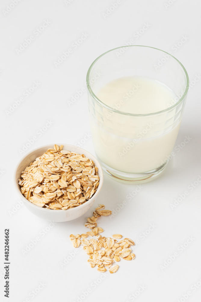 Oats as popular ingredient for variant of vegetable milk. Dry, raw oat flakes in boul and milk in a glass ingredients for making oatmeal porridge on white background Oats as popular ingredient for variant of vegetable milk. Dry, raw oat flakes in boul and milk in a glass ingredients for making oatmeal porridge on white background
